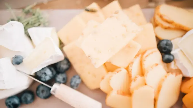 Sliced cheeses on a wooden board with blueberries