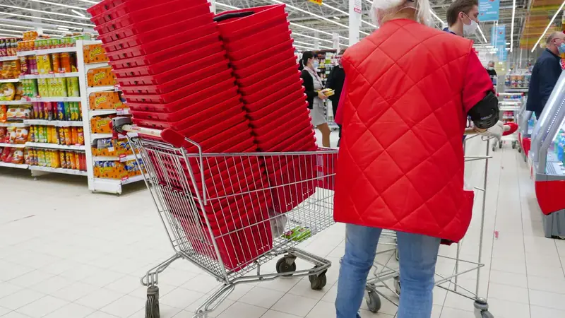 A shopper in a red vest pushing a cart past stacked red shopping baskets